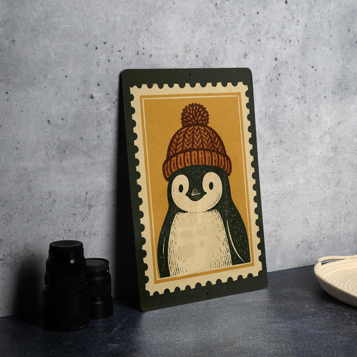 A framed illustration of a penguin wearing a winter hat is displayed on a gray wall.