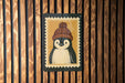 A penguin wearing a knitted hat is depicted on a sign against a wooden background.