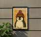 A penguin wearing a knitted hat is depicted on a sign, which is mounted on a wall.