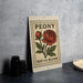 A decorative metal sign with a floral design and text, placed on a table next to some black camera lenses.