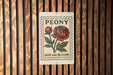 A sign with the word "PEONY" and a large red flower is displayed against a wooden background.