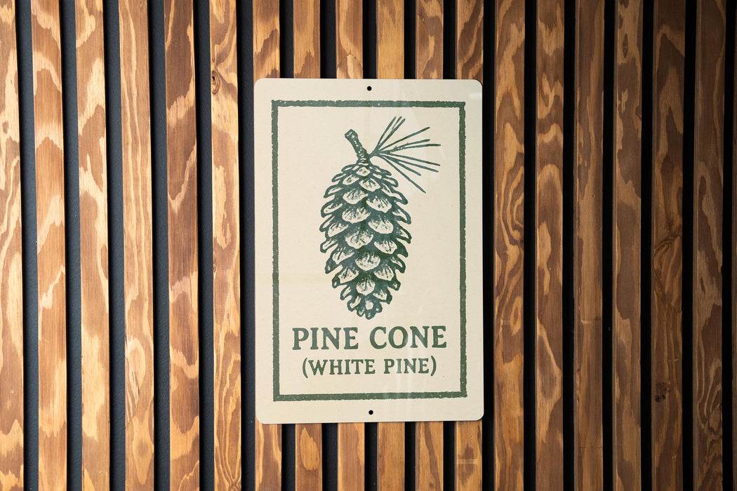 A sign with a pine cone illustration is mounted on a wooden wall.