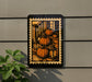 A framed illustration of pumpkins on a porch is displayed on a wall, with a plant visible to the left.