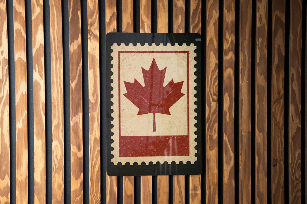 A red maple leaf is displayed on a wooden wall, mounted on a black border.
