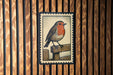 A postage stamp featuring a colorful illustration of a bird perched on a wooden fence.