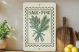 a kitchen counter with a decorative sign that reads "Sage + Pine" and a potted plant to the left. There is also a wooden cutting board and a bunch of lemons on the counter.