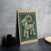 a wooden animal, possibly a goat, with a green and beige border, standing on a gray surface.