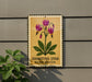 A sign with a yellow background and a picture of purple flowers is mounted on a gray wall.