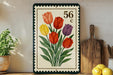 A framed illustration of a bouquet of colorful tulips is displayed on a shelf, accompanied by a wooden cutting board and a potted plant.