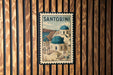 A vintage postage stamp featuring the iconic architecture of Santorini, Greece, with the text "SANTORINI" prominently displayed.