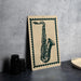 a framed illustration of a saxophone on a wall, with a stack of black camera lenses placed next to it.