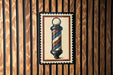 A framed image of a barber pole is displayed on a wooden wall.