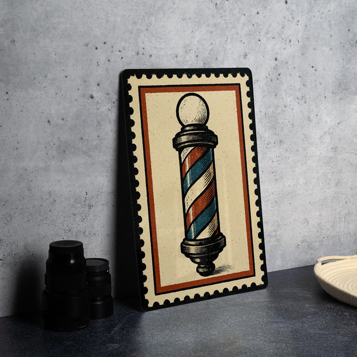 A framed illustration of a barber pole is displayed on a countertop, accompanied by a stack of black camera lenses and a white dish.
