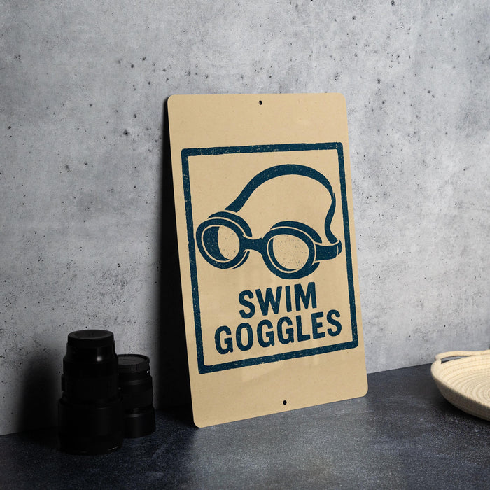 A sign with the text "SWIM GOGGLES" and an illustration of swim goggles is displayed on a table.