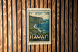 A framed poster of Waipio Valley overlooking the ocean, mounted on a wooden wall.