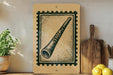 a wooden frame with a stamp-like design on it, placed on a shelf next to a potted plant and a wooden cutting board.