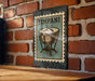 A metal sign with a stamp-like design hangs on a brick wall, featuring an illustration of a drum or cymbal.