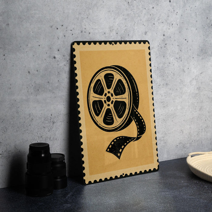 a framed artwork depicting a film reel on a wall, with a stack of black camera lenses placed next to it.