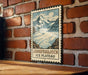 A vintage-style metal sign with a mountain landscape and a river, mounted on a brick wall.