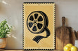 a framed artwork depicting a film reel on a shelf, surrounded by kitchen utensils and a potted plant.