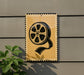 a sign with a film reel graphic on it, mounted on a wall next to a plant.