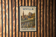 A vintage postage stamp from Spain, featuring the Seville Cathedral, is displayed on a wooden wall.