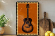 a framed picture of an acoustic guitar on a shelf, with a potted plant to the left and a wooden cutting board to the right.
