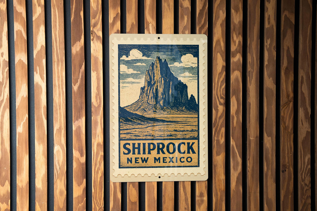 A vintage-style postage stamp featuring a mountain landscape with the text "SHIPROCK NEW MEXICO" printed on it, mounted on a wooden wall.