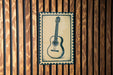 A framed image of a guitar is displayed on a wooden wall.