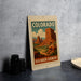 A framed poster of the Grand Canyon in Colorado, featuring a scenic illustration of the red rock country landscape.