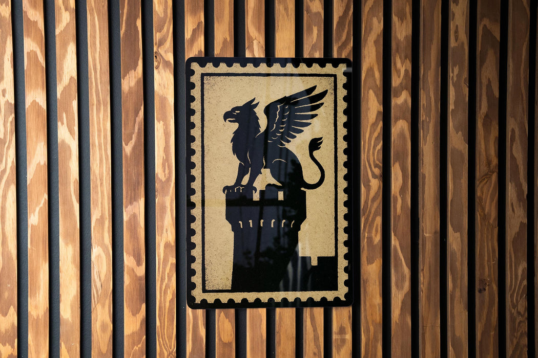 A black and gold emblem featuring a winged lion is displayed on a wooden wall.