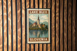 A vintage postage stamp from Slovenia depicting a church and a lake, hanging on a wooden wall.