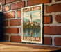 A vintage-style metal sign with a painting of a church and a lake, mounted on a brick wall.