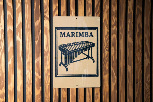 a sign with the word "MARIMBA" and an illustration of a musical instrument, specifically a xylophone, mounted on a wooden wall.
