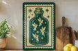 a green and white sign with a whimsical illustration of fairies inside a bottle, surrounded by stars and a cork. The sign is displayed on a shelf next to a wooden cutting board and a potted plant.
