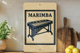 a wooden sign with a black and white illustration of a musical instrument, specifically a marimba, and the word "MARIMBA" written on it. The sign is placed on a wooden surface, with a potted plant to the left and a cutting board to the right. There are also some lemons visible in the image.