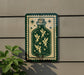 a green and gold sign with a fairy illustration on it, mounted on a wall next to a plant.