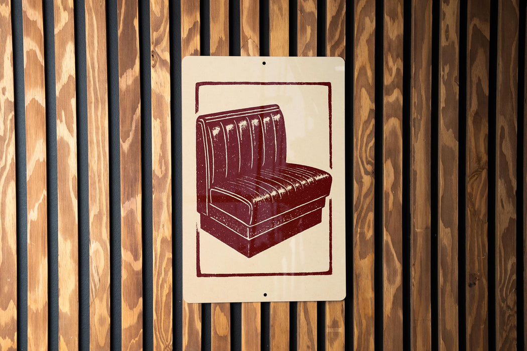 a red and white sign with a graphic of a booth or booth-like structure, mounted on a wooden wall.