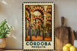a framed poster of the Cordoba Cathedral in Spain, with a wooden cutting board and a potted plant to the left.