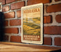 A metal sign with the text "NEBRASKA SANDHILLS COUNTRY" is displayed on a brick wall.