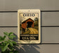 A sign that reads "OHIO COVERED BRIDGE USA 20c" is displayed on a wall, with a plant to the left of the sign.