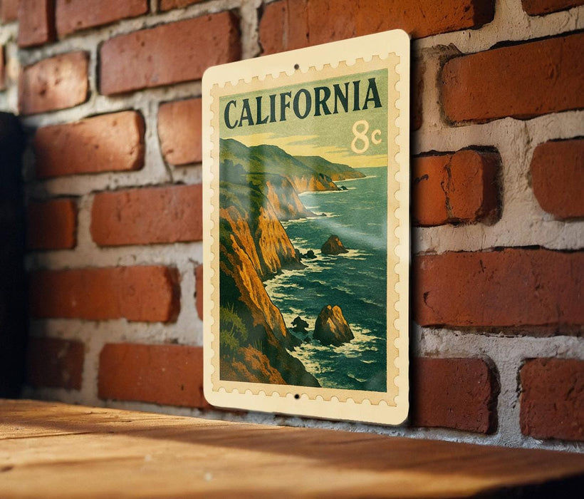 A vintage California postage stamp is displayed on a brick wall, featuring a scenic coastal landscape with mountains and ocean.