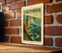 A vintage California postage stamp is displayed on a brick wall, featuring a scenic coastal landscape with mountains and ocean.