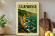 A framed vintage postage stamp depicting a scenic coastal landscape in California, with mountains, cliffs, and the ocean in the background.