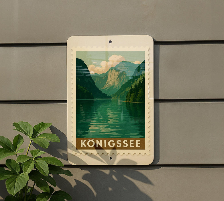 A framed image of a mountain landscape with a lake is displayed on a wall, with a plant to the left of the frame.