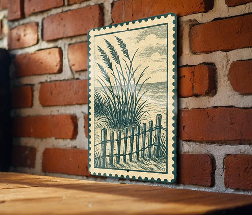 A framed illustration of tall grasses and a wooden fence is displayed on a brick wall.