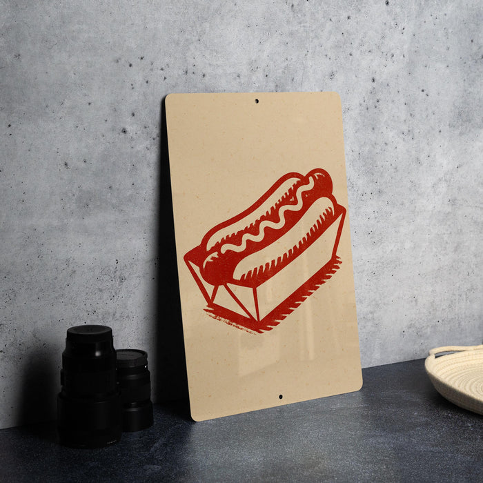a sign with a red hot dog illustration on it, placed on a table next to some black containers.