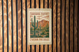 A wooden wall with a framed poster of a desert landscape featuring cacti and mountains.