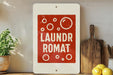 A red and white sign with the text "Laundromat Romat" is displayed on a shelf, accompanied by a wooden cutting board and a potted plant.