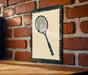A framed tennis racket is hanging on a brick wall, with a wooden table below it.